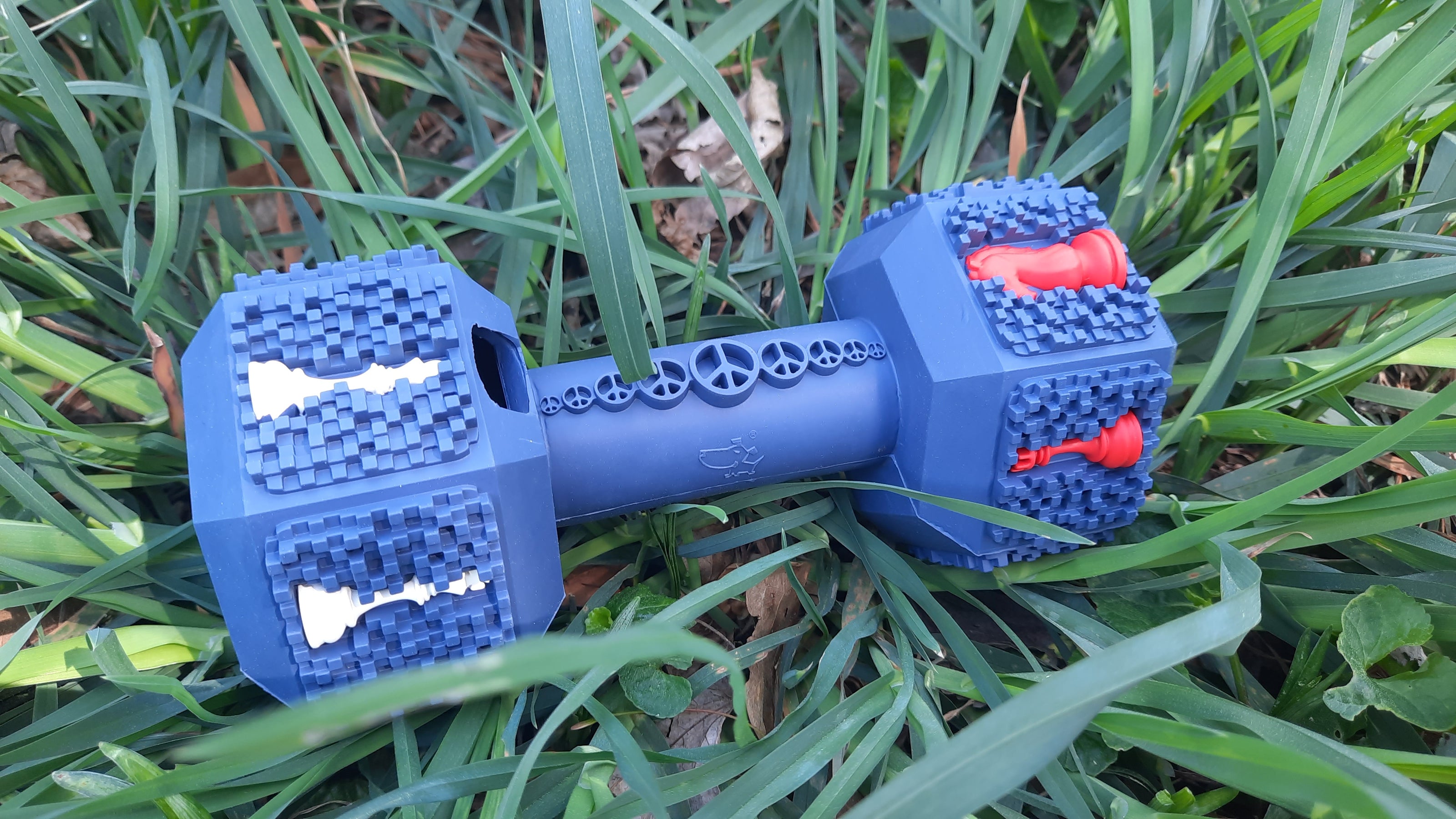 Our large version of the dumbbell toy laying in the grass in a close-up shot. The blue rubber chew toy is brand new, not having been used.