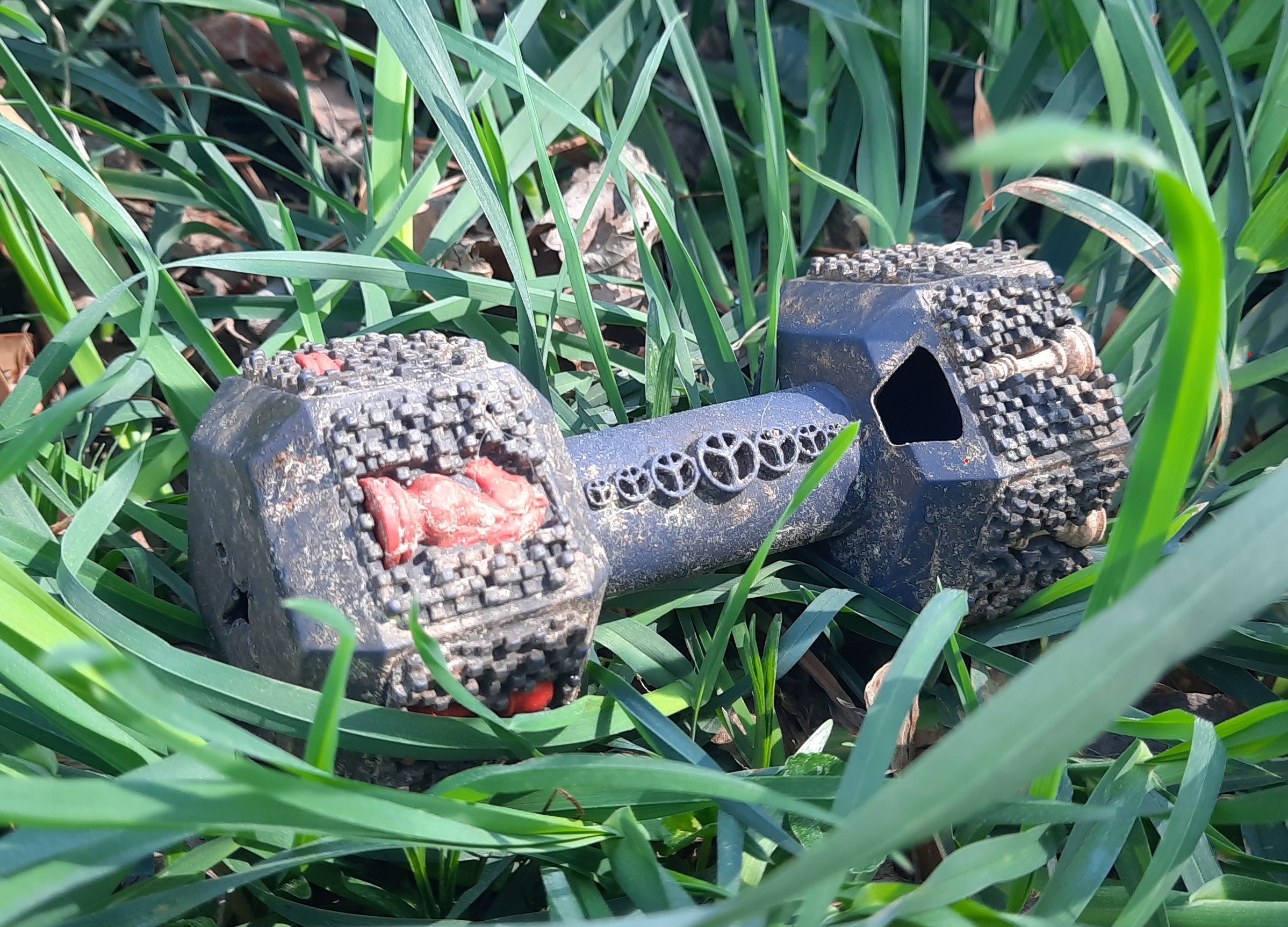 Our rubber chew toy laying in the grass in a close-up picture. The dumbbell toy is covered in dirt from the overuse. But It has no damage, showing how durable it is.